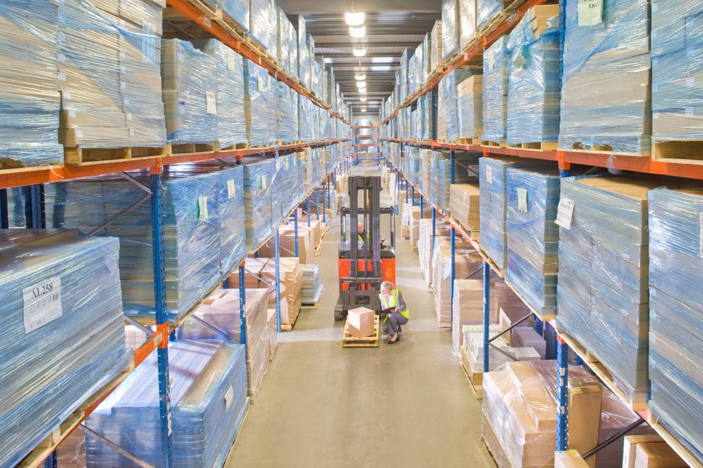 Logistics warehouse with stacked pallets, storage racks and workers coordinating stock movement