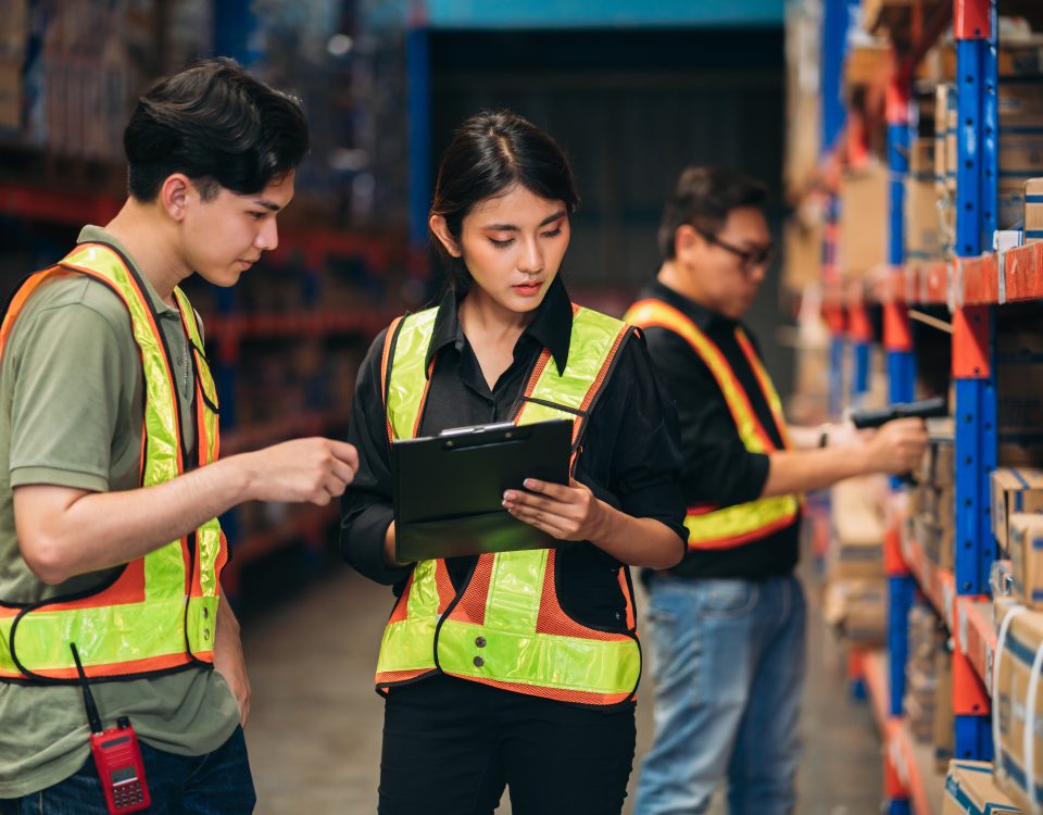 Warehouse staff reviewing inventory records while checking goods on storage racks